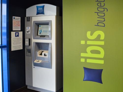an atm machine is next to a green wall at ibis budget Vannes in Vannes