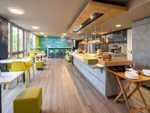 a restaurant with a counter and tables and yellow chairs at ibis budget Rennes Chantepie - Hôtel rénové in Chantepie
