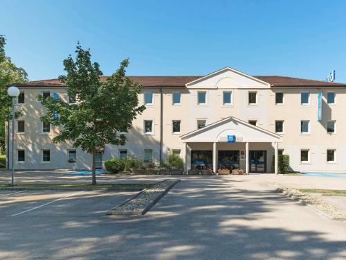 a large white building with a tree in front of it at ibis Budget Lons-le-Saunier in Lons-le-Saunier