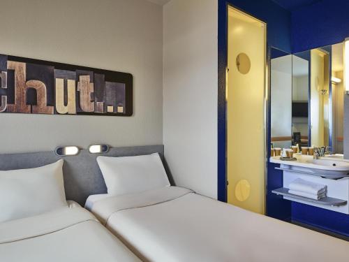 a hotel room with two beds and a sink at Ibis Budget Vélizy in Vélizy-Villacoublay