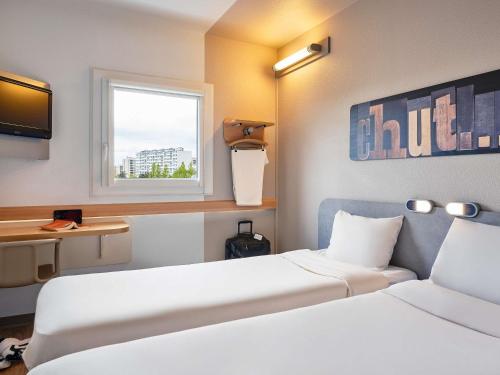 a hotel room with two beds and a window at Ibis Budget Vélizy in Vélizy-Villacoublay