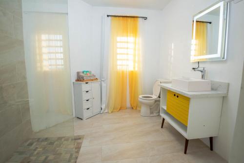 a bathroom with a sink and a toilet and yellow curtains at The Hidden Cottage in Welches Hill