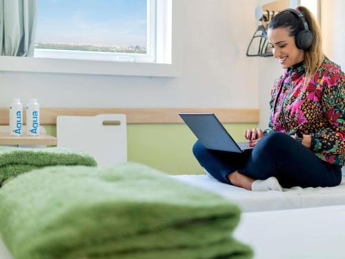 a woman sitting on a bed with a laptop and headphones at ibis budget Sao Paulo Jardins in Sao Paulo