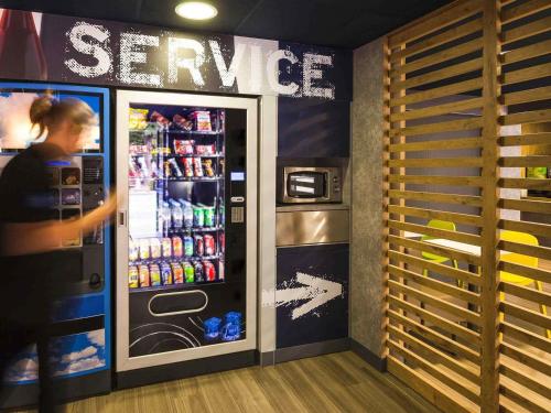 a woman standing in front of a soda machine at Hotel ibis Budget Laval in Bonchamp-lès-Laval