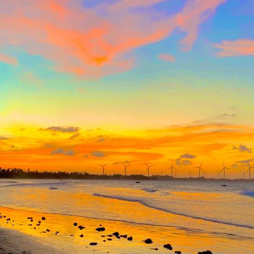 a sunset on a beach with windmills in the background at Casa Peroá Pousada in Icaraí