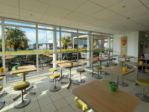 a cafeteria with tables and chairs and large windows at Ibis Budget Ancenis in Mésanger