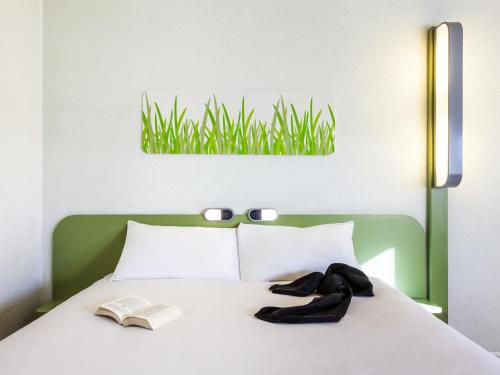 a bedroom with a bed with a book and grass on the wall at ibis budget Orange Centre in Orange