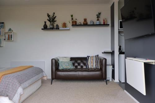 a living room with a leather couch and a bed at Barrique Studio with Sauna at Barrelled Wines Raglan in Raglan