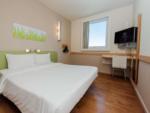 a hotel room with a large white bed and a desk at ibis budget Vitoria in Vitória