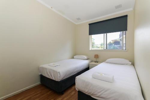two beds in a small room with a window at Scarborough Apartments in Perth