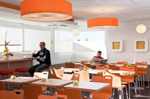 two men sitting at tables in a room with orange chairs at ibis budget Istres Trigance in Istres