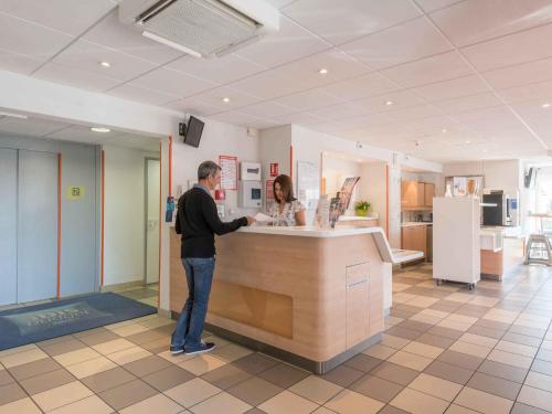 a man and a woman standing at a counter at ibis budget Amberieu en Bugey/Chateau Gaillard A42 in Château-Gaillard