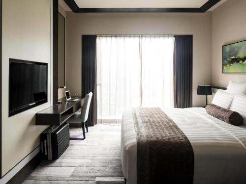 a hotel room with a bed and a desk and a television at Pullman Zhuhai in Zhuhai