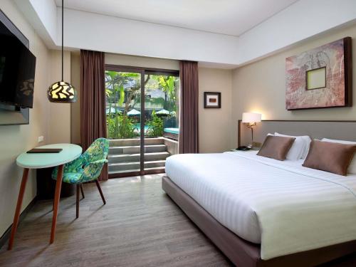 a bedroom with a large white bed and a table and chair at Mercure Bali Legian in Legian
