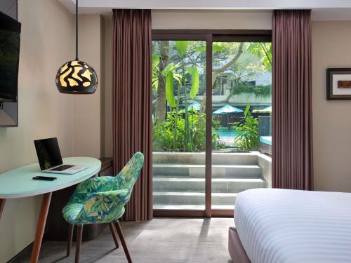 a bedroom with a bed and a desk with a laptop at Mercure Bali Legian in Legian