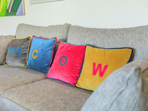 Un sofá con tres almohadas con las palabras the o y w en The Cow Shed, en Buckland St Mary
