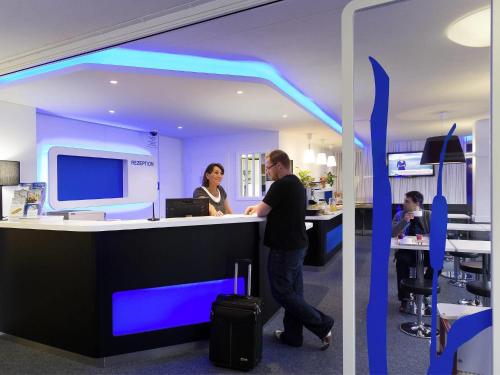 a man and a woman standing at a counter in an office at ibis budget Albertville in Gilly-sur-Isère