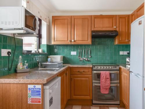 a kitchen with wooden cabinets and green tiles at Dairy Cottage - Uk49834 in Lanivet