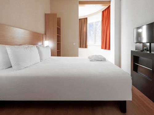 a bedroom with a large white bed and a television at Ibis Astana in Astana