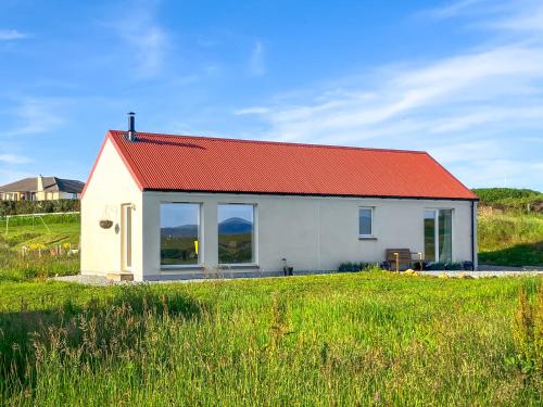a small white house with an orange roof in a field at Taigh Mullach Dearg in Portree