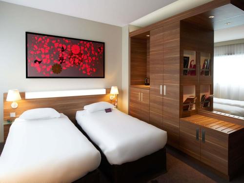 a hotel room with two beds and a painting on the wall at Mercure Cholet Centre in Cholet