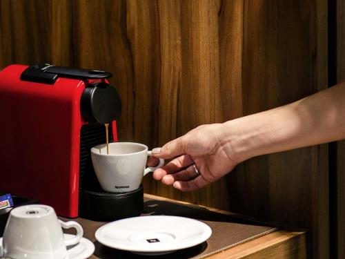 a hand is holding a coffee cup next to a coffee maker at Mercure Curitiba Batel in Curitiba