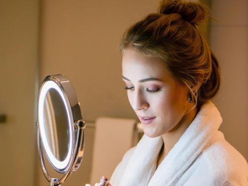 a woman looking at her face in a mirror at Mercure Curitiba Batel in Curitiba