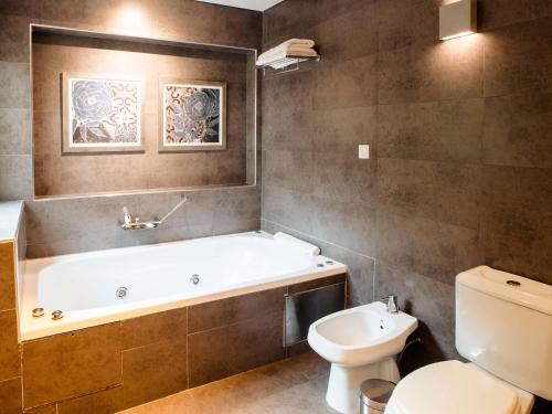 a bathroom with a bath tub and a toilet at Mercure Iguazu Hotel Iru in Puerto Iguazú