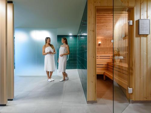 two women in white dresses standing in a bathroom at Mercure Hotel Wiesbaden City in Wiesbaden