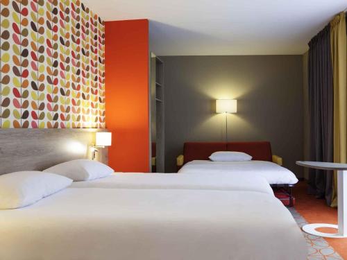two beds in a hotel room with orange walls at ibis Styles Chaumont Centre Gare in Chaumont
