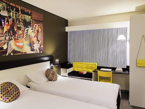a room with two beds and a desk with a yellow chair at Ibis Styles Porto Alegre Centro in Porto Alegre