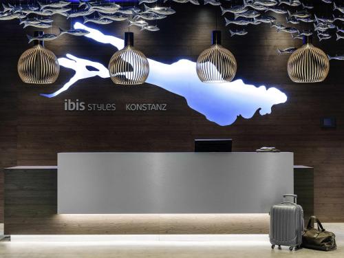 a reception desk with a suitcase and pendant lights at Ibis Styles Konstanz in Konstanz
