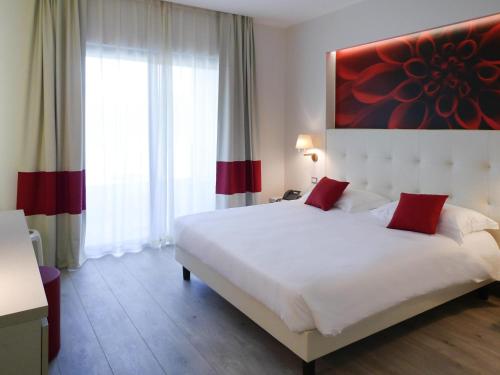 a bedroom with a large white bed with red pillows at ibis Styles Milano Est Settala in Settala