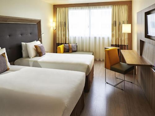 a hotel room with two beds and a desk and a window at Novotel Rio de Janeiro Parque Olimpico in Rio de Janeiro