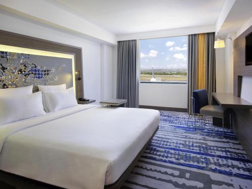 a hotel room with a large bed and a desk at Novotel Bali Ngurah Rai Airport in Kuta