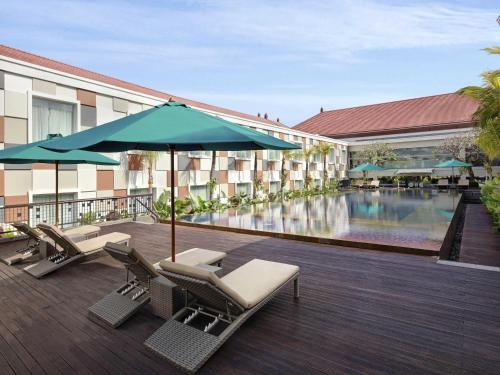 a hotel with a pool and chairs and an umbrella at Novotel Bali Ngurah Rai Airport in Kuta