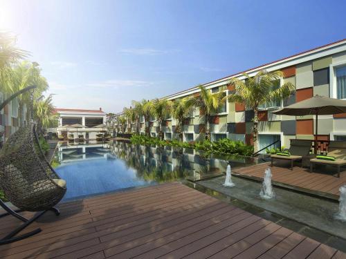 a hotel with a swimming pool and palm trees at Novotel Bali Ngurah Rai Airport in Kuta