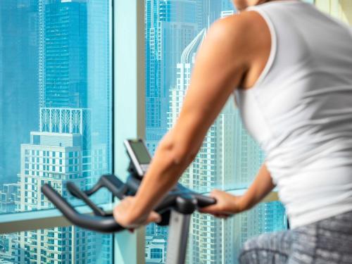 a woman riding an exercise bike in front of a city at Pullman Dubai Jumeirah Lakes Towers in Dubai