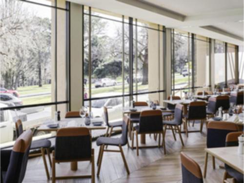 a dining room with tables and chairs and windows at Pullman Melbourne On the Park in Melbourne