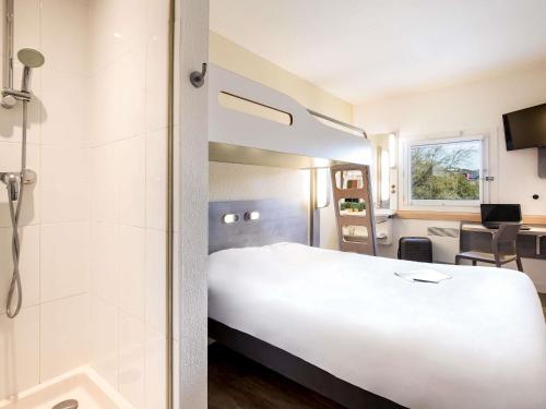 a hotel room with a large white bed and a bathroom at Ibis Budget Fréjus Capitou in Fréjus