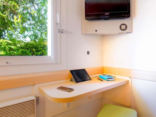 a room with a desk with a tv and a window at Ibis Budget Fréjus Capitou in Fréjus