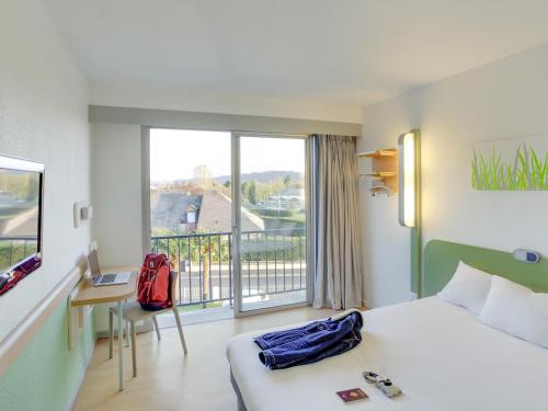 a hotel room with a bed and a desk and a window at ibis budget Pau Lescar in Lescar