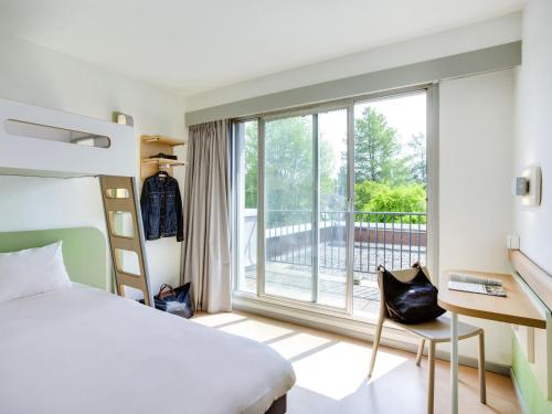 a bedroom with a bed and a large window at ibis budget Pau Lescar in Lescar