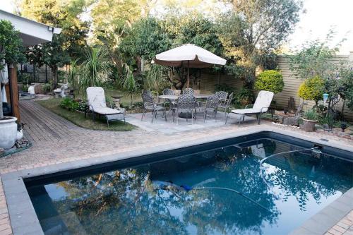 a swimming pool with chairs and a table and an umbrella at 79 On Ridge Bed and Breakfast in Pietermaritzburg