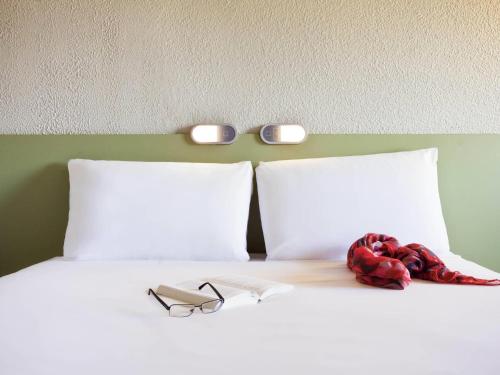 a bed with two pillows and a pair of glasses on it at Ibis Budget Sisteron in Sisteron