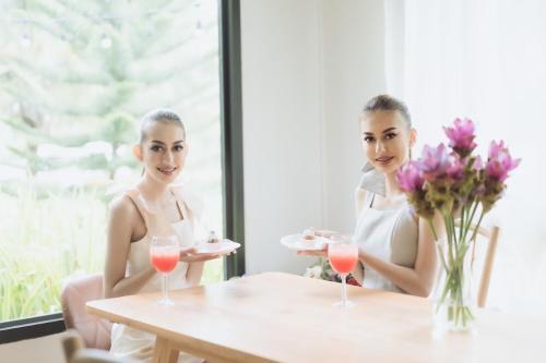 zwei Frauen sitzen an einem Tisch mit Weingläsern in der Unterkunft Payim farm พายิ้มฟาร์ม in Ban Nam Khrai