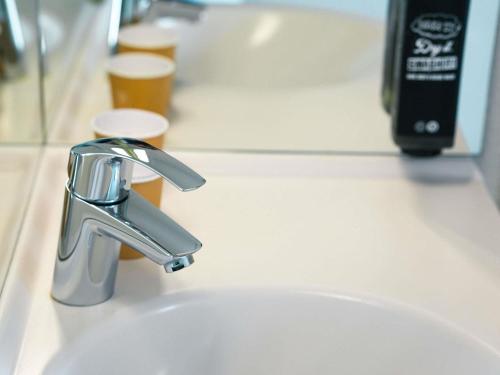 a sink with a faucet and two glasses of beer at ibis budget Caen Porte de Bretagne in Bretteville-sur-Odon