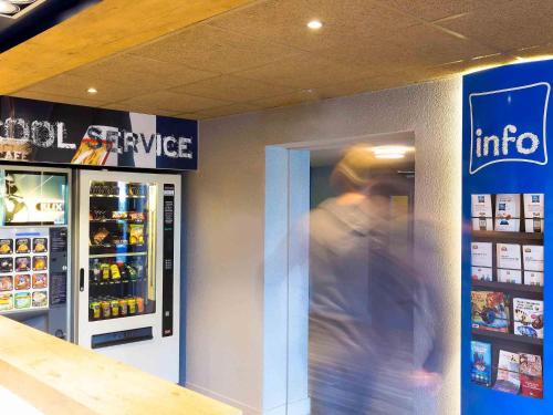 a man is walking past a cooler in a store at Ibis budget Lorient Caudan in Caudan