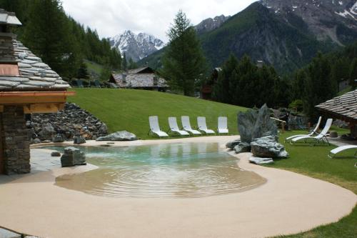 a pool in a yard with chairs and mountains at Eco Wellness Hotel Notre Maison in Cogne
