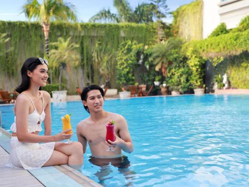 two people sitting in a swimming pool with drinks at Grand Mercure Medan Angkasa in Medan